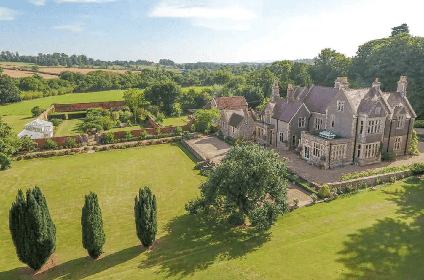 An aerial shot of a 17 century castle surrounded by green fields, private garden and lush trees